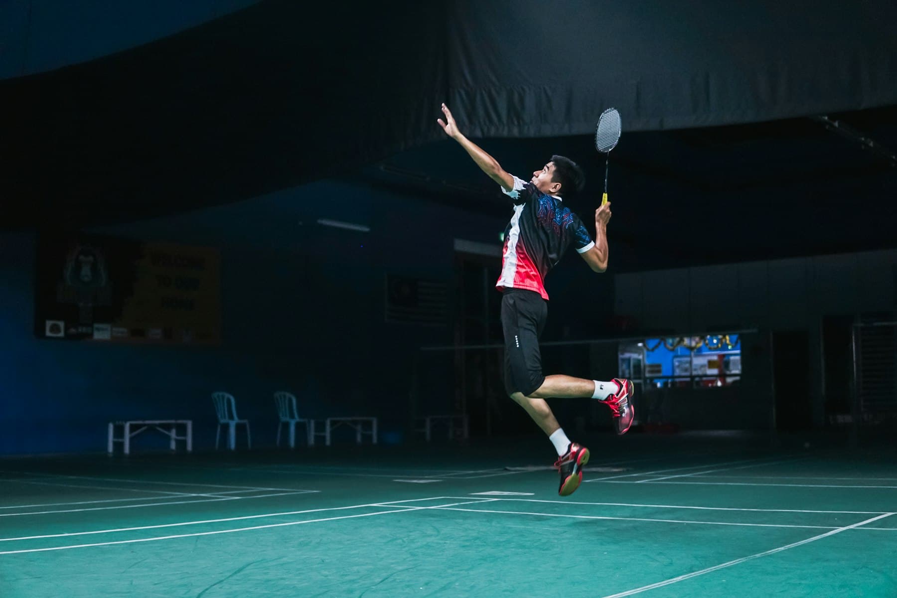 A badminton player airborne mid-smash on a floodlit indoor court